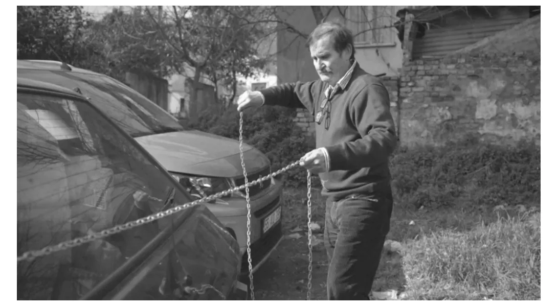 Foto van een man in een trui die een zware ketting vasthoudt naast een geparkeerde auto.