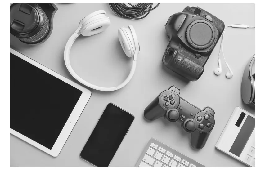 Foto van een bovenaanzicht van spullen op een grijs oppervlak: koptelefoon, telefoon, een camera, een game-controller en een tablet.