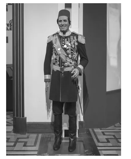 Foto van een wassen beeld van een man in een versierd donker uniform met een fes op het hoofd en een sabel.