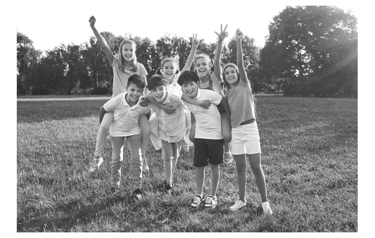Foto van een groep lachende jongeren die op een grasveld hun armen in de lucht steken.