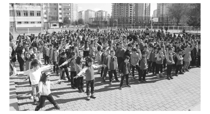 Foto van een groot aantal leerlingen op een schoolplein die tegelijk bewegen.