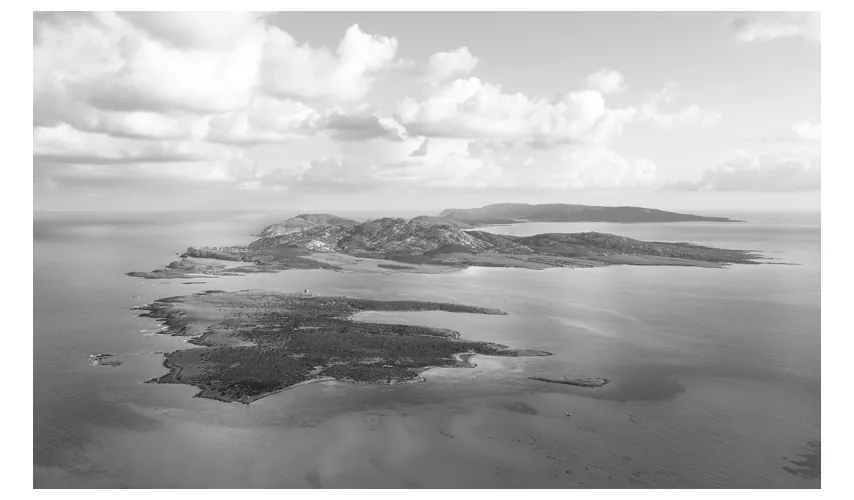 Luchtfoto van een eiland met kustlijnen en een zee met rustig water onder een bewolkte lucht.