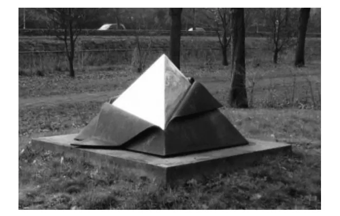 Kunstwerk op een betonnen sokkel in een park: een glanzende stalen piramide met daaromheen een donkere laag cortenstaal die aan de voorkant openvouwt.